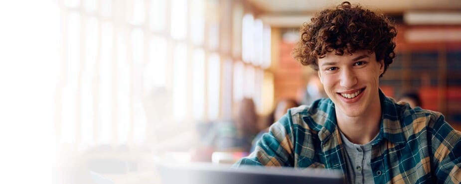 Smiling young man using laptop in bright library